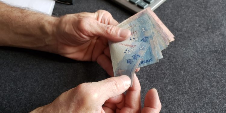 hands of an older man holding brazilian banknotes